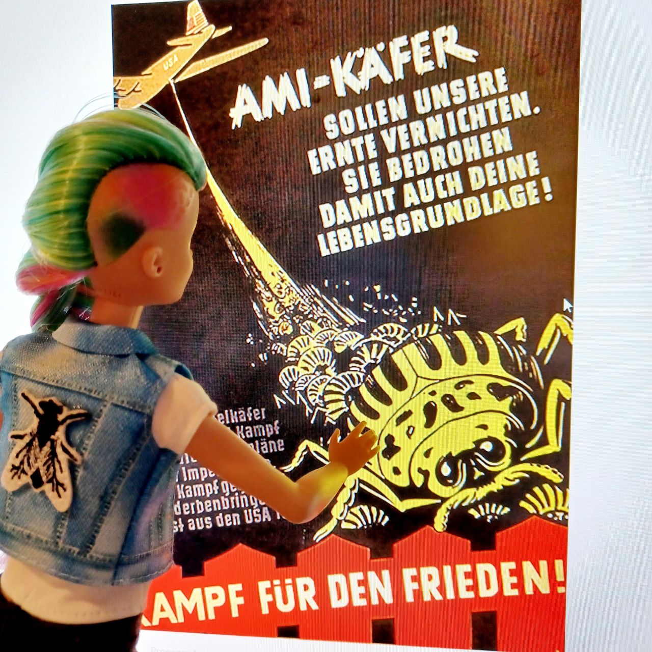 Eine Punk-Barbie-Puppe betrachtet ein Propagandaplakat.